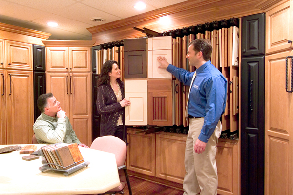 A franchisee shows cabinet design options to two clients in a showroom.