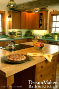 A kitchen remodel with brown wooden cabinets, flowers on the countertops, a bowl of apples and oranges and a freshly made pastry cooling on the kitchen island.