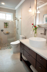 A bathroom with white tile walls and floors, a white counter with a raised sink, and brown cabinets.