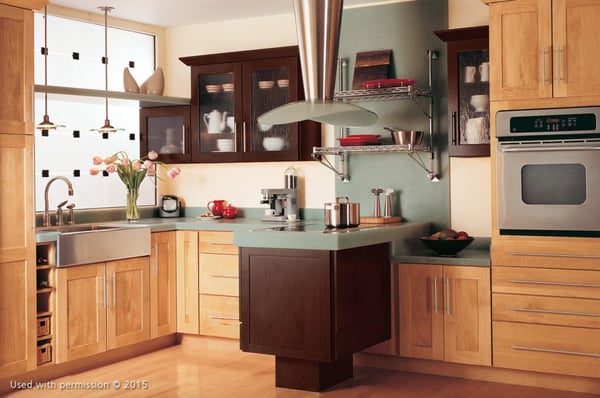 A modern kitchen remodel, with light wooden cabinet fronts and flooring, a dark-brown stovetop and faded teal countertops.