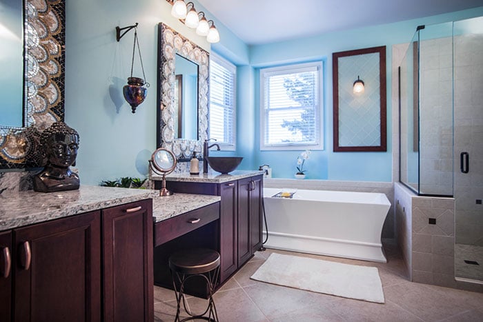 A bathroom remodel with sky-blue walls, brown cabinets with marble countertops and a separate bathtub and shower.