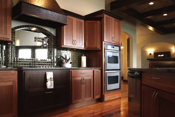 A kitchen design with dark wood cabinets and hardwood floors, with a forest green tile backsplash along the wall.