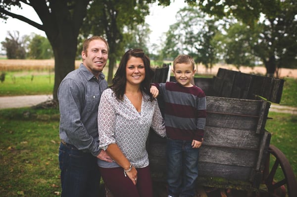 Franchisee Jay Nutting and his wife and son pose for a family photo near a wooden wagon in a field.