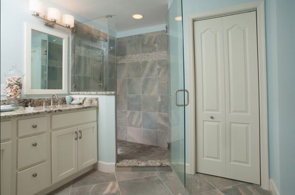 A view of a bathroom remodel with gray tiles on the floor and walk-in shower, off-white doors and cabinets and light blue walls.
