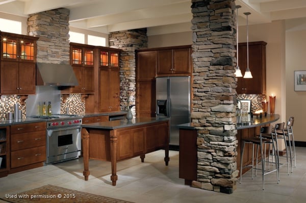 A kitchen remodel with stone columns, hardwood cabinets, an off-white tile floor and dark gray countertops.