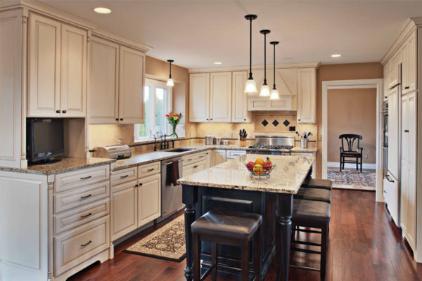 An image of a recent kitchen remodel, with white cabinets around the wall and pendant lights hanging over the dark-wood, marble-topped center island.